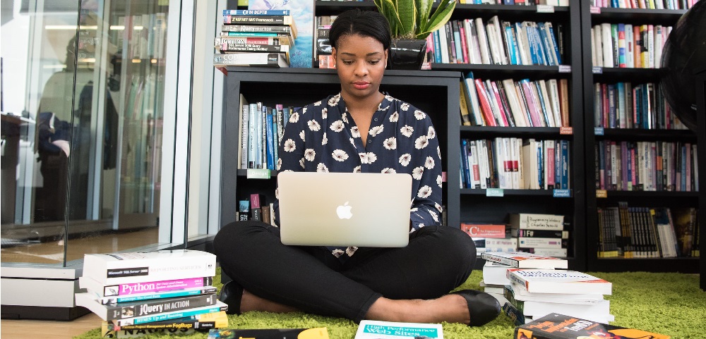 Innovation Academy Woman sitting on the floor, surround by books, and working on a laptop