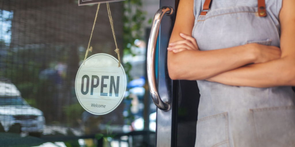 The woman is a waitress in an apron, the owner of the cafe stands at the door with a sign Open waiting for customers. Small business concept, cafes and restaurants
