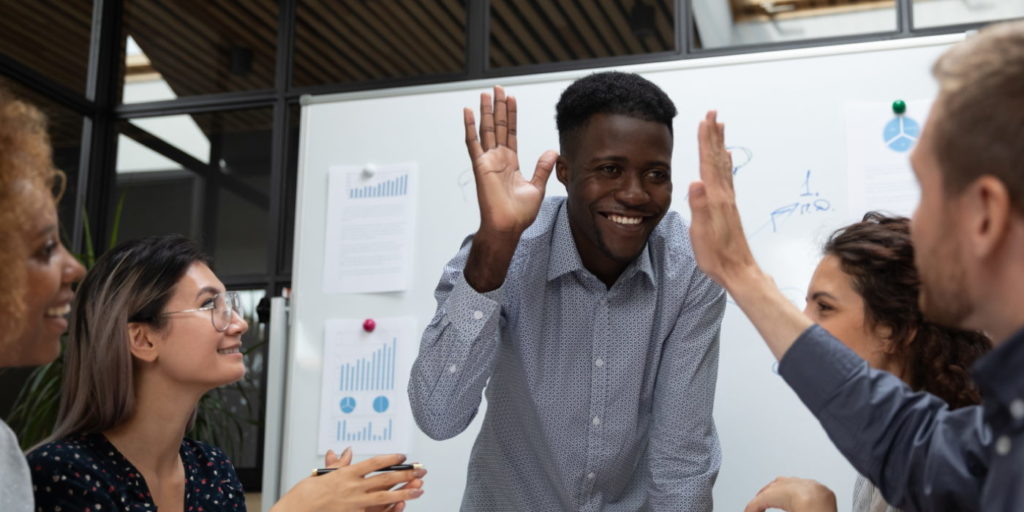 Happy african american team leader raising hand, giving high five to caucasian partner, investor or teammate at business people meeting in office. Mixed race young employees discussing project ideas.